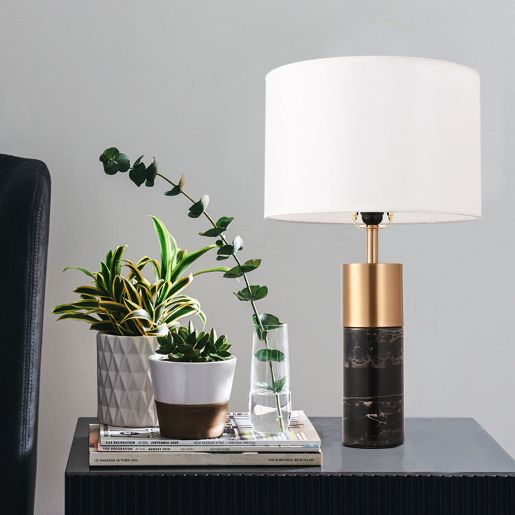 Table lamp with gold and black base on a table with plants and books against a gray wall.